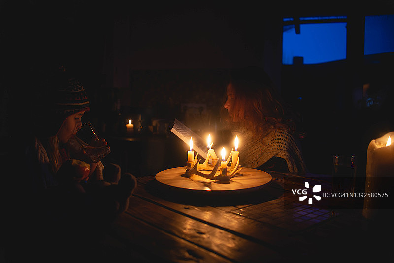 能源危机，缺少暖气和电力，孩子和母亲穿着暖和的衣服，在家中点着蜡烛。图片素材