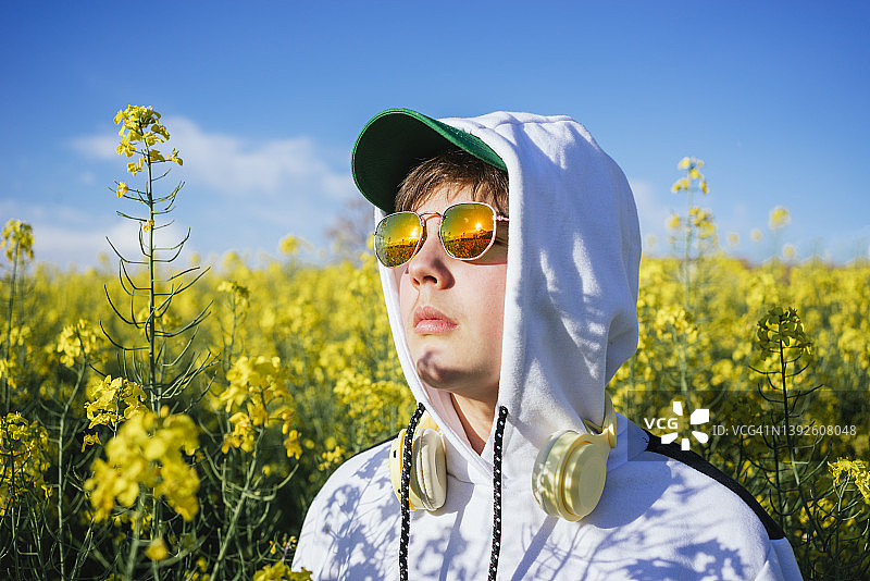 青少年男孩在黄色花田中身穿帽衫和太阳镜的肖像照图片素材