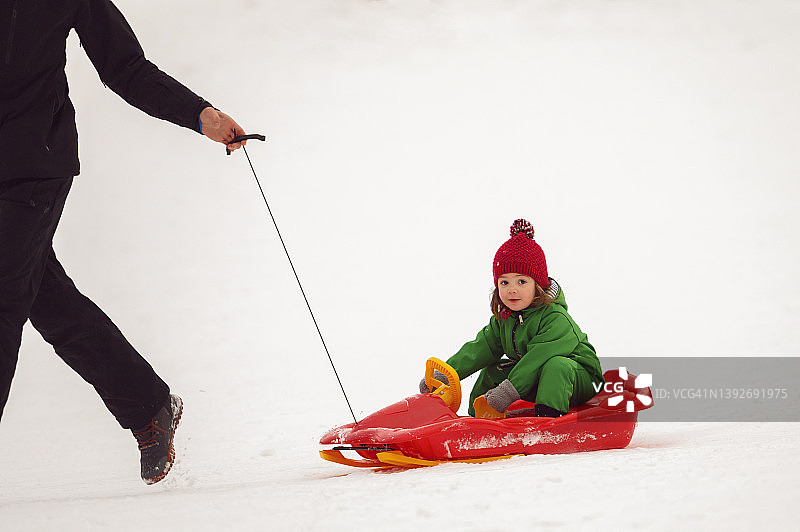 父亲在雪山上拉着女儿坐雪橇图片素材