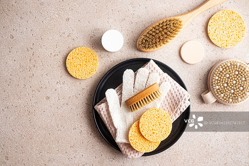 环保身体护理必需品（木制身体刷、清洁手套、清洁海绵、精华素瓶、发刷、保湿霜）和混凝土背景上的毛巾。家庭水疗，平放。零浪费概念。图片素材