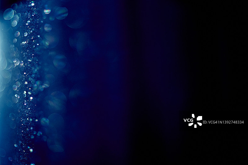 蓝色背景，光线中闪耀的圆形小尘埃颗粒图片素材