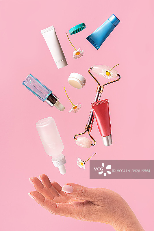 女人手持飞行中的护肤品，粉色背景图片素材