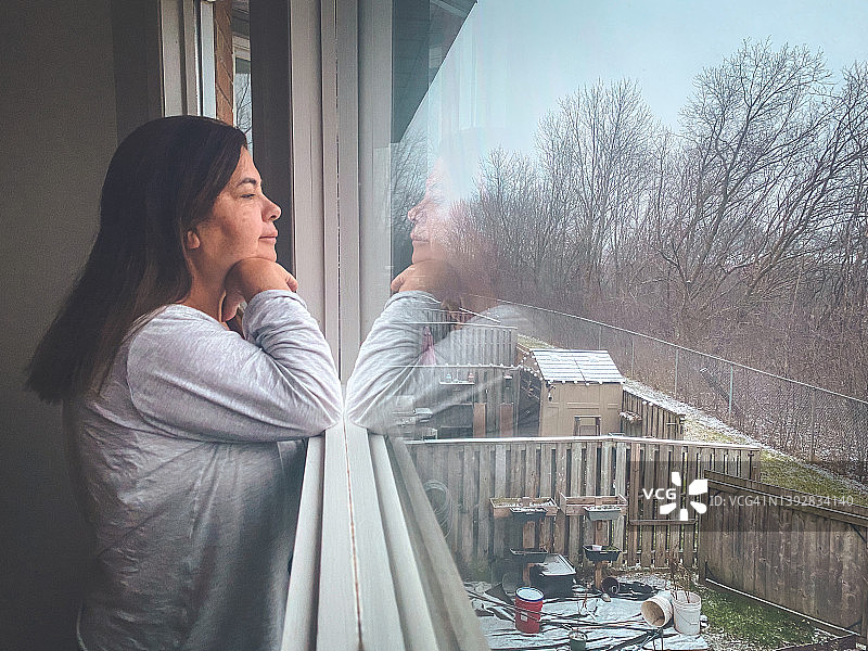 侧视角度拍摄的女子，以及她看着窗外飘雪的倒影图片素材