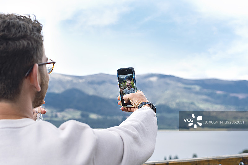 年轻的拉丁裔游客在旅行和探索内乌萨水库时，在度假期间用智能手机在自然环境中自拍。图片素材