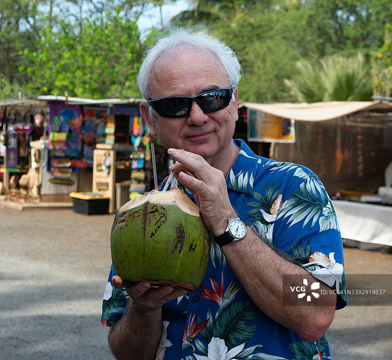 男子站在美国夏威夷毛伊岛的市场里喝新鲜椰子汁图片素材