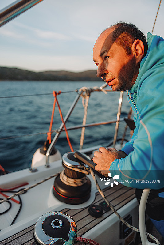 棕色短发水手摇动曲柄绞盘收回帆，坐在帆船甲板上，阳光照在他的脸上图片素材