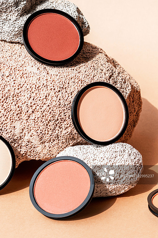 米色背景上的粉饼、腮红和眼影，垂直构图图片素材