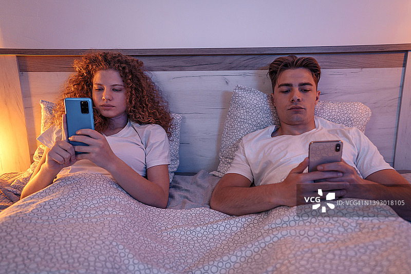 情侣晚上躺在床上使用智能手机图片素材