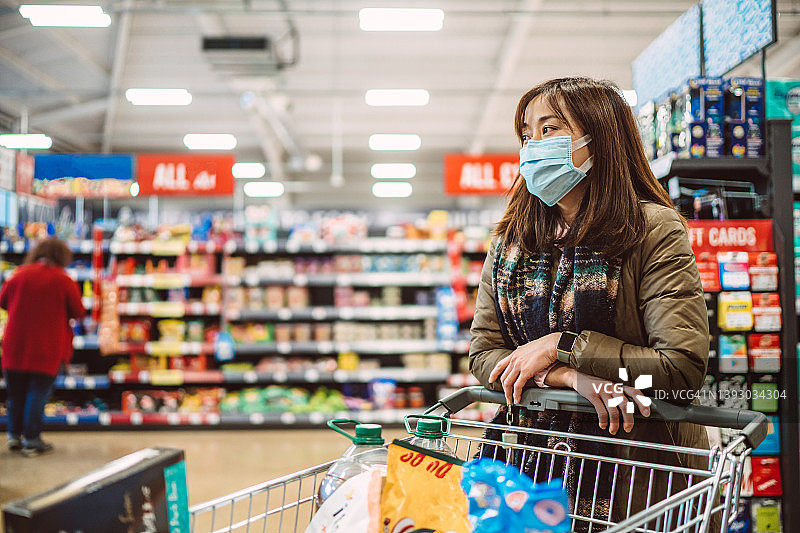 戴着防护口罩在超市购买日常食品的年轻亚裔女性图片素材