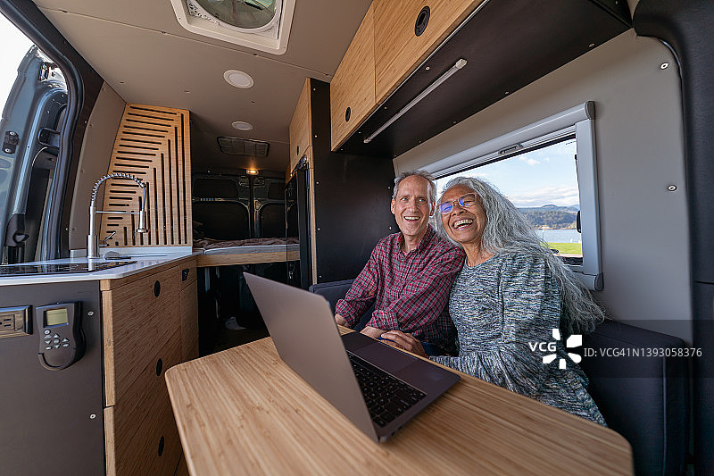 充满活力的年长夫妇在露营车中旅行时使用笔记本电脑图片素材