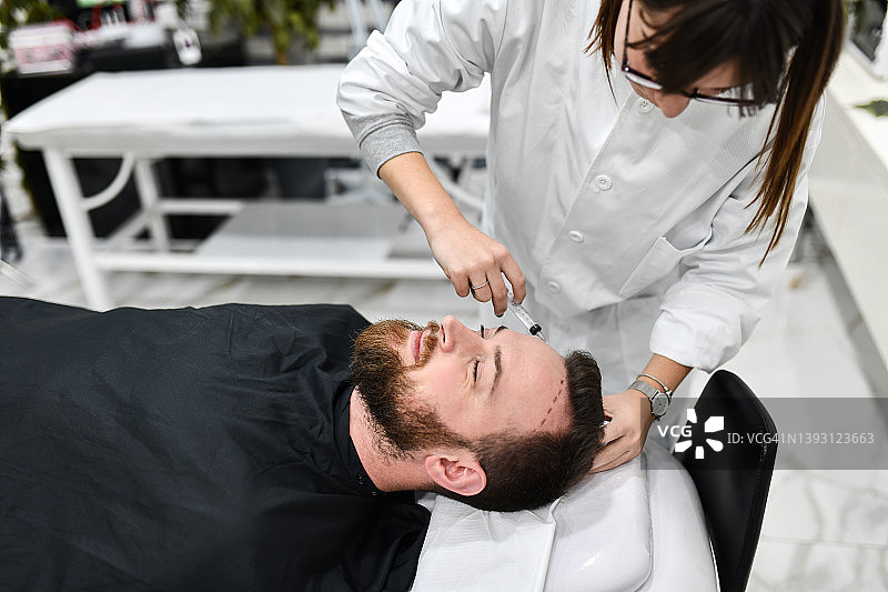 男性在诊所放松，女性美容外科医生标记发际线图片素材