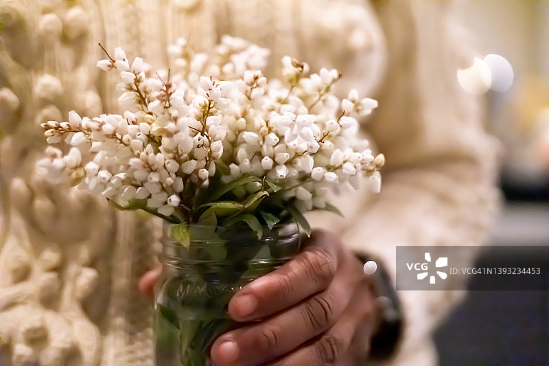 黑人女性在室内手捧装在玻璃罐里的铃兰花束图片素材