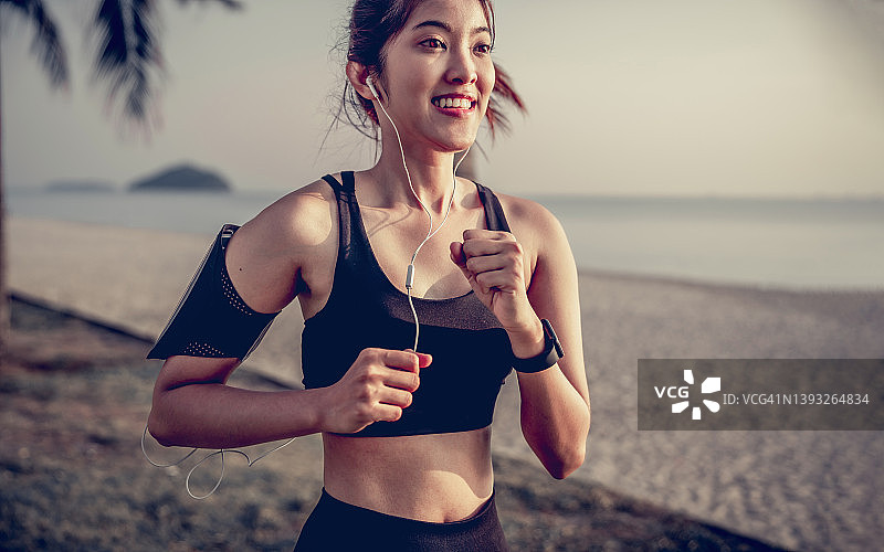 年轻的健身运动女性在公园跑步，戴着耳机在户外晨跑图片素材