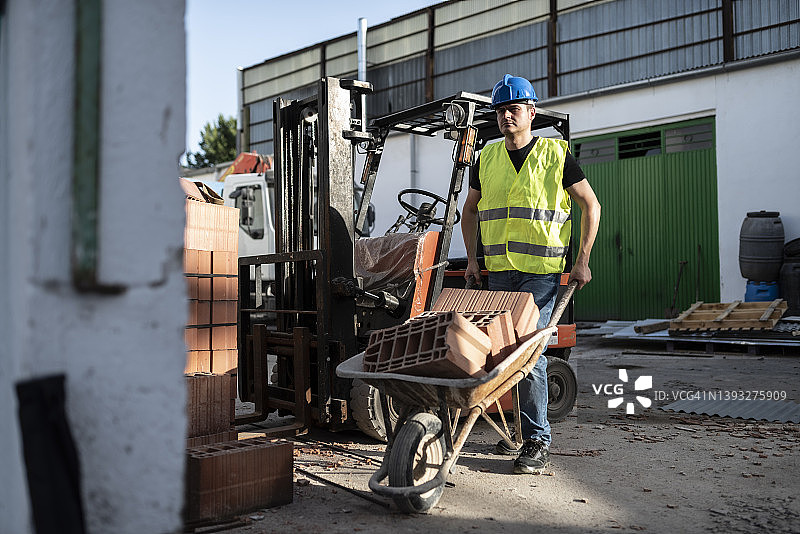 建筑工人将砖块放入手推车，工厂改造场景，工作中的男人图片素材