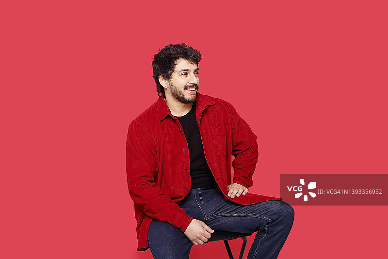 留着胡须、身穿红色纽扣衬衫和蓝色牛仔裤的巴基斯坦千禧一代男人肖像，背景是纯红色图片素材