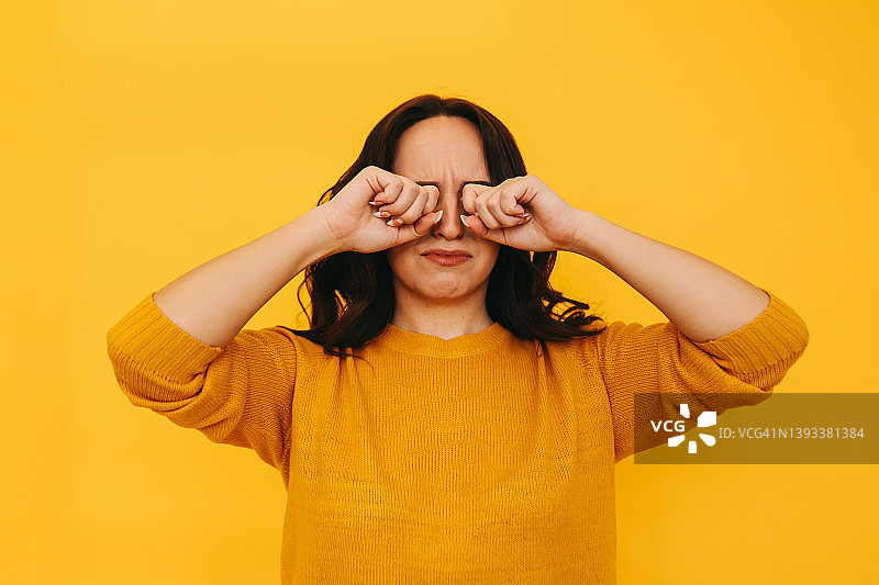 黄色背景中哭泣并用手捂住眼睛的悲伤女孩图片素材