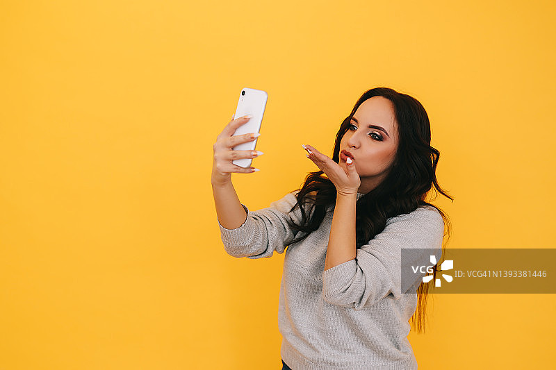 快乐的年轻女子在黄色背景上用手机进行视频聊天图片素材