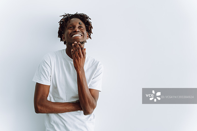 自信微笑的黑人爆炸头男士看着镜头，摸着下巴，笑着抬头，站在白色背景前图片素材