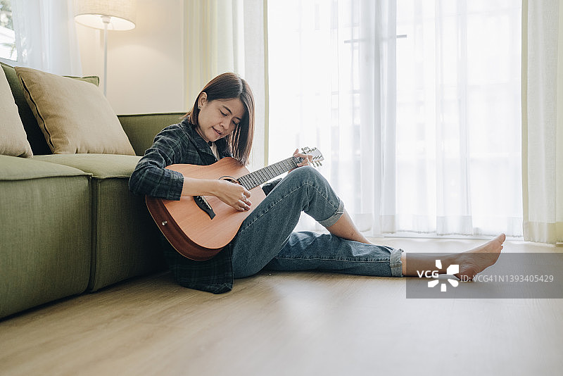 年轻亚洲女子在客厅沙发上弹吉他图片素材