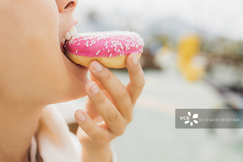 一位饥饿的肥胖妇女正在咬甜甜圈的特写。不健康的快餐饮食的概念。无法辨认的人。图片素材