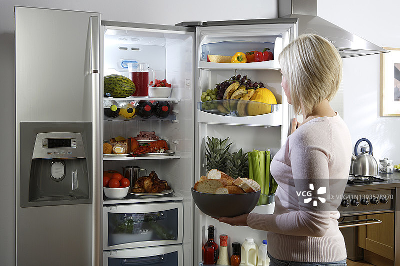 年轻女子在厨房打开冰箱查看食物和饮料图片素材