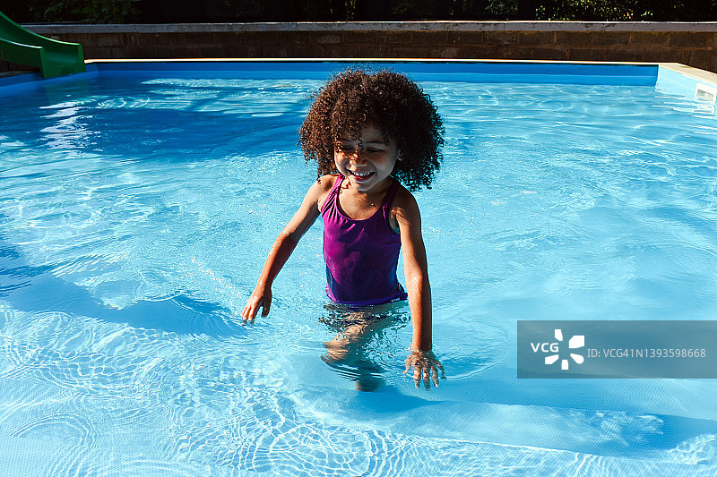 穿着紫色泳衣的黑皮肤小女孩在泳池里游泳图片素材