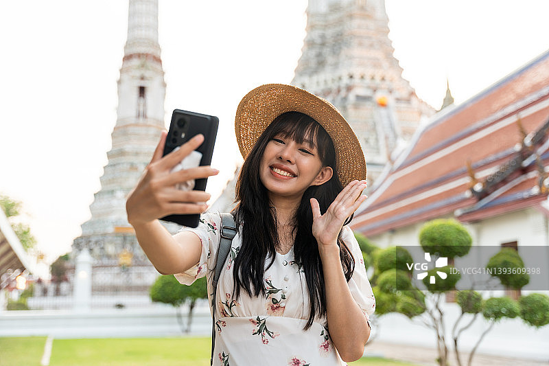 在泰国曼谷郑王庙旅行时用智能手机拍照的快乐亚洲年轻女性图片素材