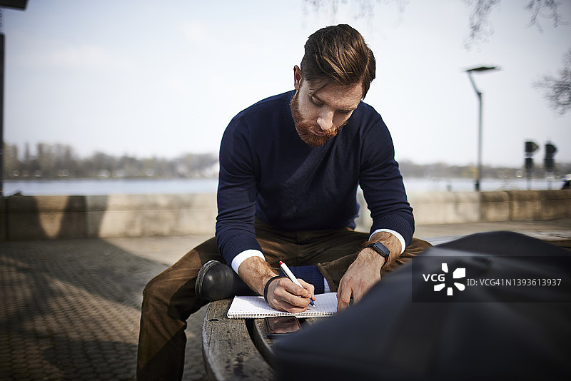 坐在长椅上做笔记的年轻男人图片素材