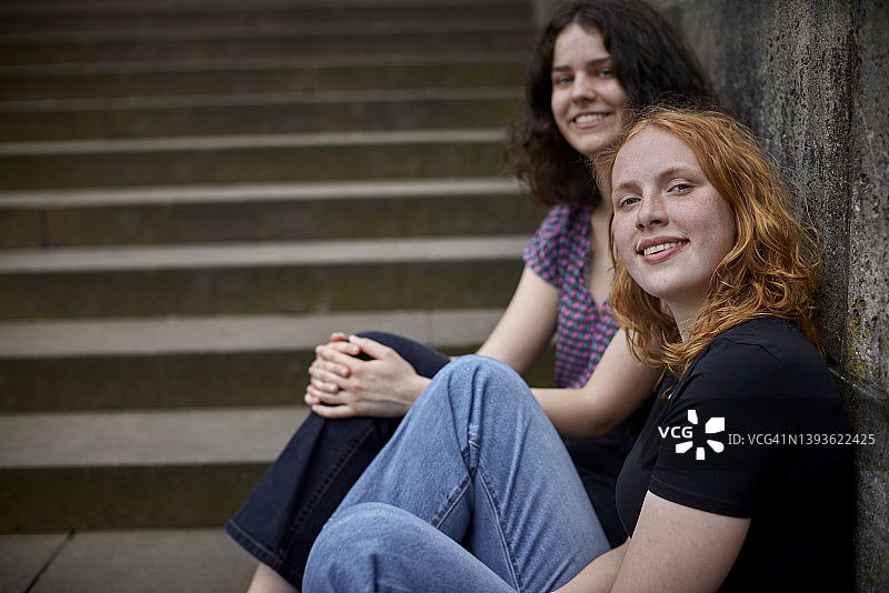 两个微笑的女性朋友坐在墙边的肖像图片素材