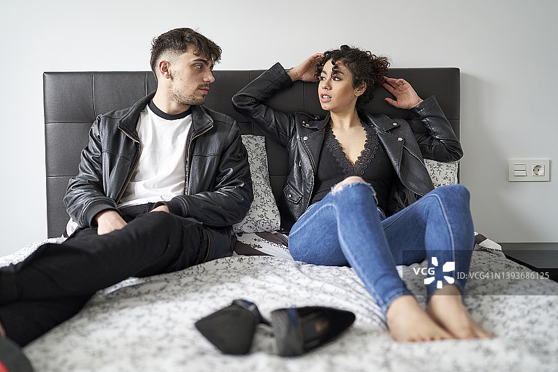 情侣坐在房间的床上，准备和朋友们一起穿着皮夹克去俱乐部跳舞图片素材