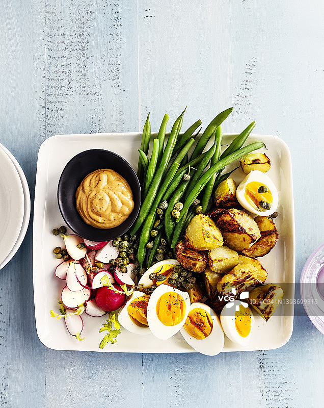 木制蓝色背景上的开胃菜拼盘（青豆、萝卜、煮鸡蛋和蒜泥烤土豆）图片素材