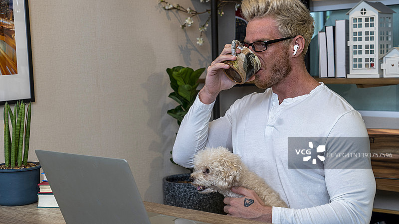 男人在家工作，膝盖上有一只可爱的小狗图片素材