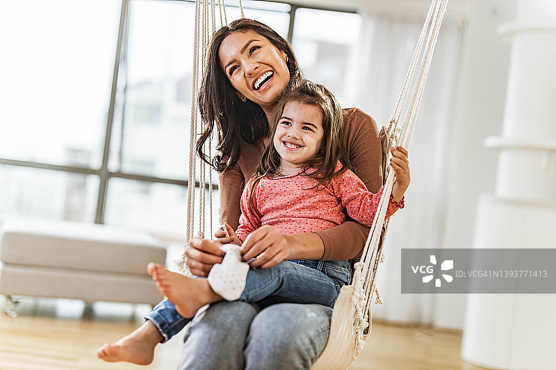 快乐的小女孩和她的单亲妈妈在家里的秋千上玩耍图片素材