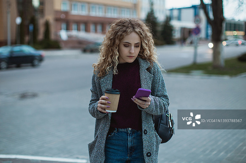 手持咖啡和手机的金发卷发女孩图片素材