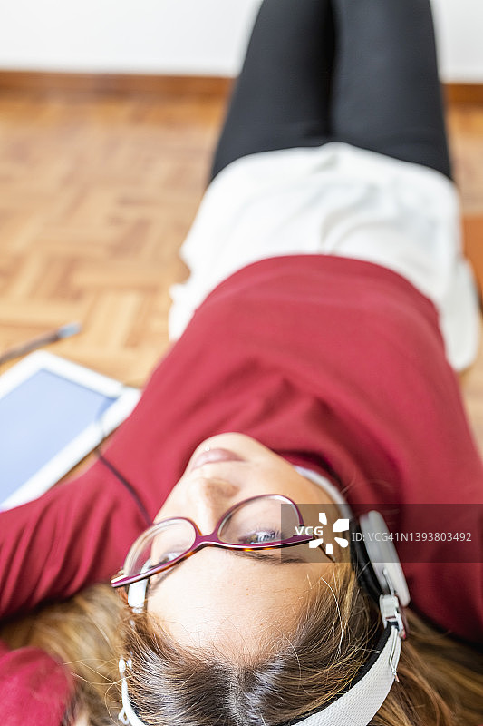 戴着耳机躺在木地板上的忧郁的年轻女人图片素材