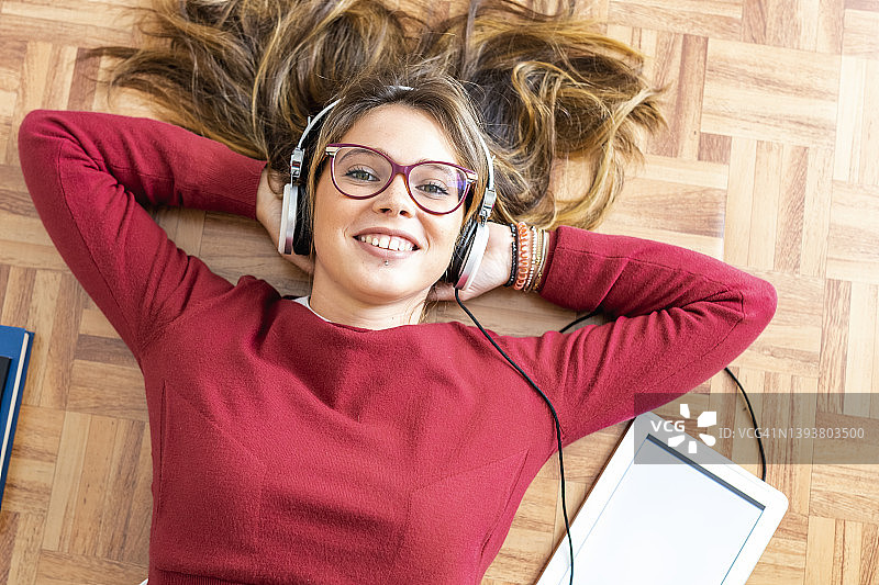 年轻女人戴着耳机躺在木地板上听音乐图片素材