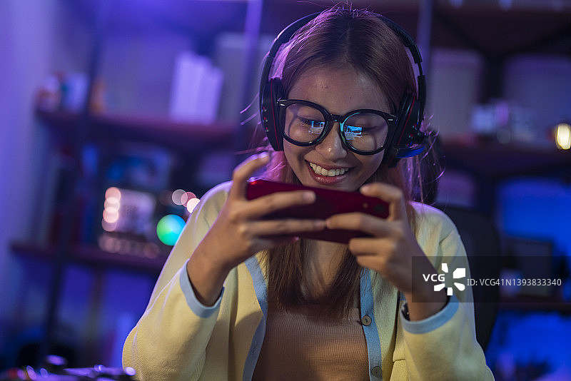 快乐的亚洲女孩戴着耳机用智能手机参加电竞比赛图片素材