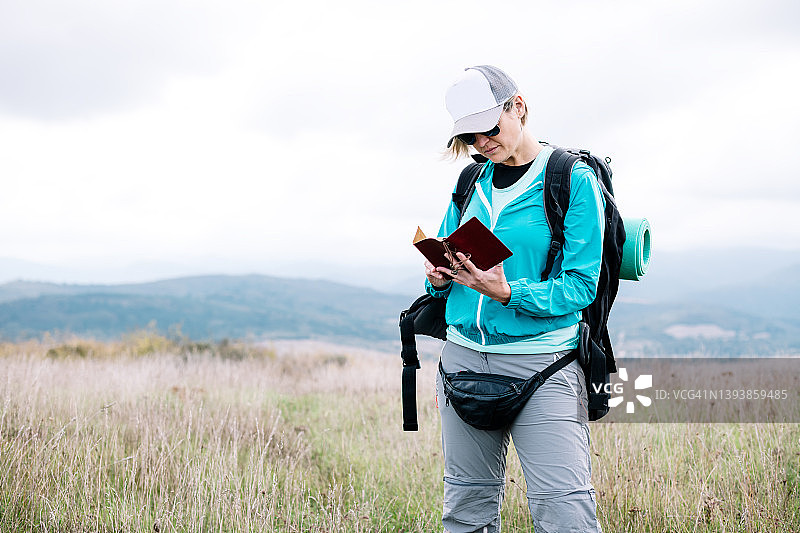 游牧女人在自然环境中背着背包阅读个人笔记本图片素材