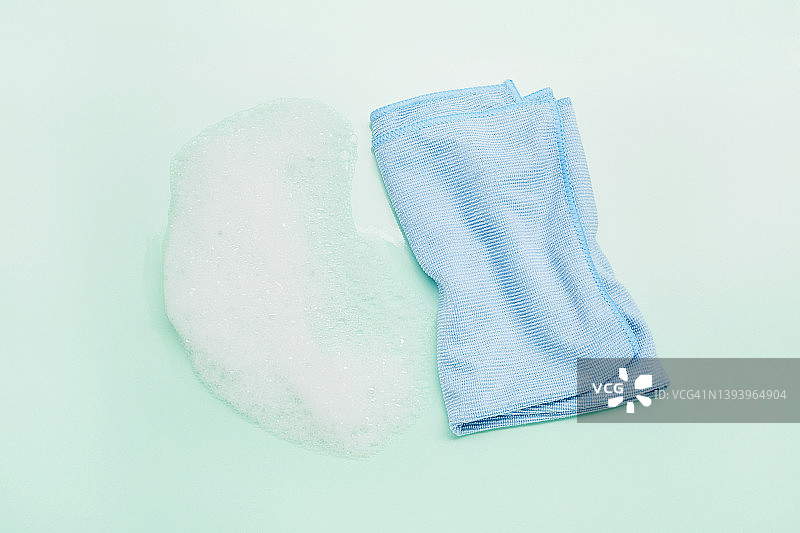 绿松石背景上的蓝色清洁布和白色泡沫高角度景观图片素材