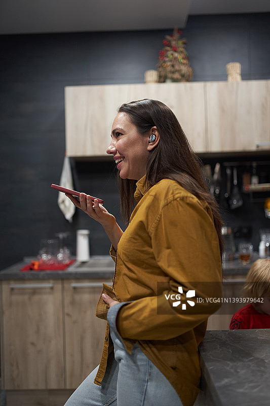 在厨房录制语音信息的快乐棕发女孩图片素材