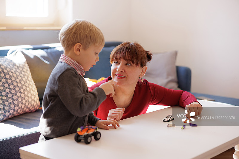 金发小男孩和妈妈在桌旁玩玩具车图片素材