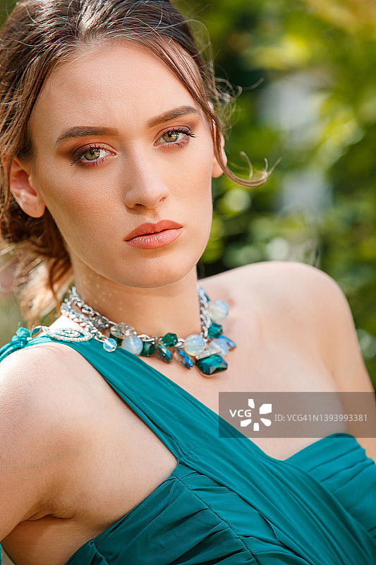 身穿祖母绿色上衣、佩戴珠宝并看着镜头的年轻漂亮女子图片素材