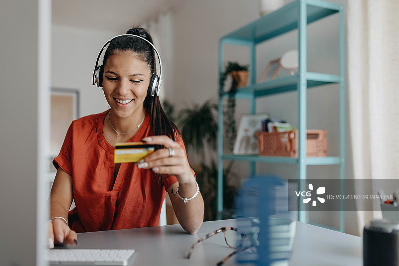 年轻漂亮的女人在家用电脑上网，戴着耳机听音乐并进行在线支付图片素材