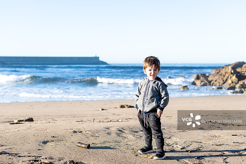 站在沙滩上看着镜头，背景是海洋的小男孩图片素材