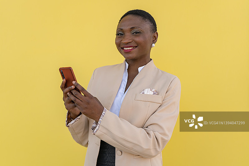 使用手机的微笑的非裔美国女商人肖像，背景为黄色图片素材