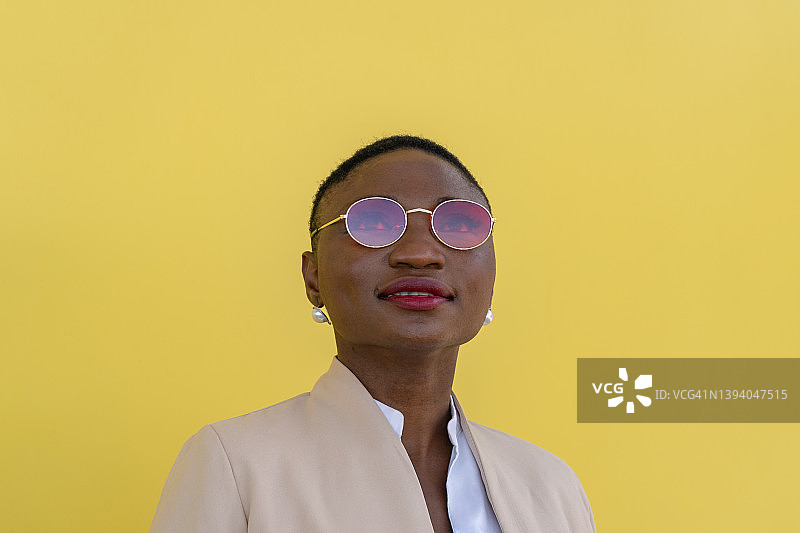 时尚的非洲裔女性肖像，戴着红色太阳镜，站在黄色背景前图片素材