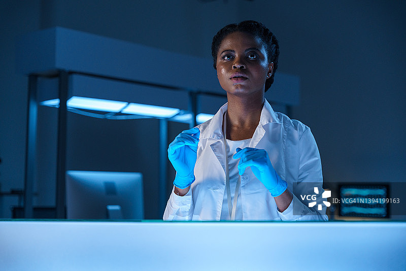 一位年轻的非洲裔美国女医学研究员身穿实验服，若有所思地望向远方图片素材