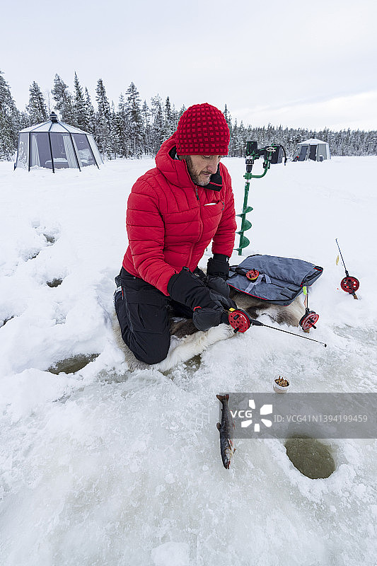 男人在瑞典拉普兰的冰冻湖面上凿洞冰钓图片素材