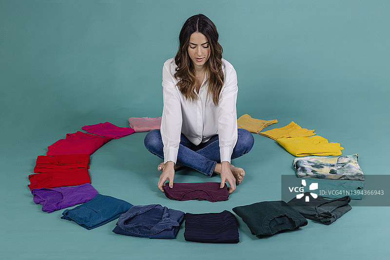 年轻女人在蓝色背景的衣服中盘腿坐着叠紫色T恤图片素材