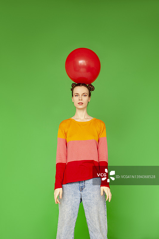 头上顶着红色气球站在绿色背景前的女人图片素材